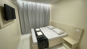 Un dormitorio moderno con cama, televisor montado en la pared y ventana con cortinas.