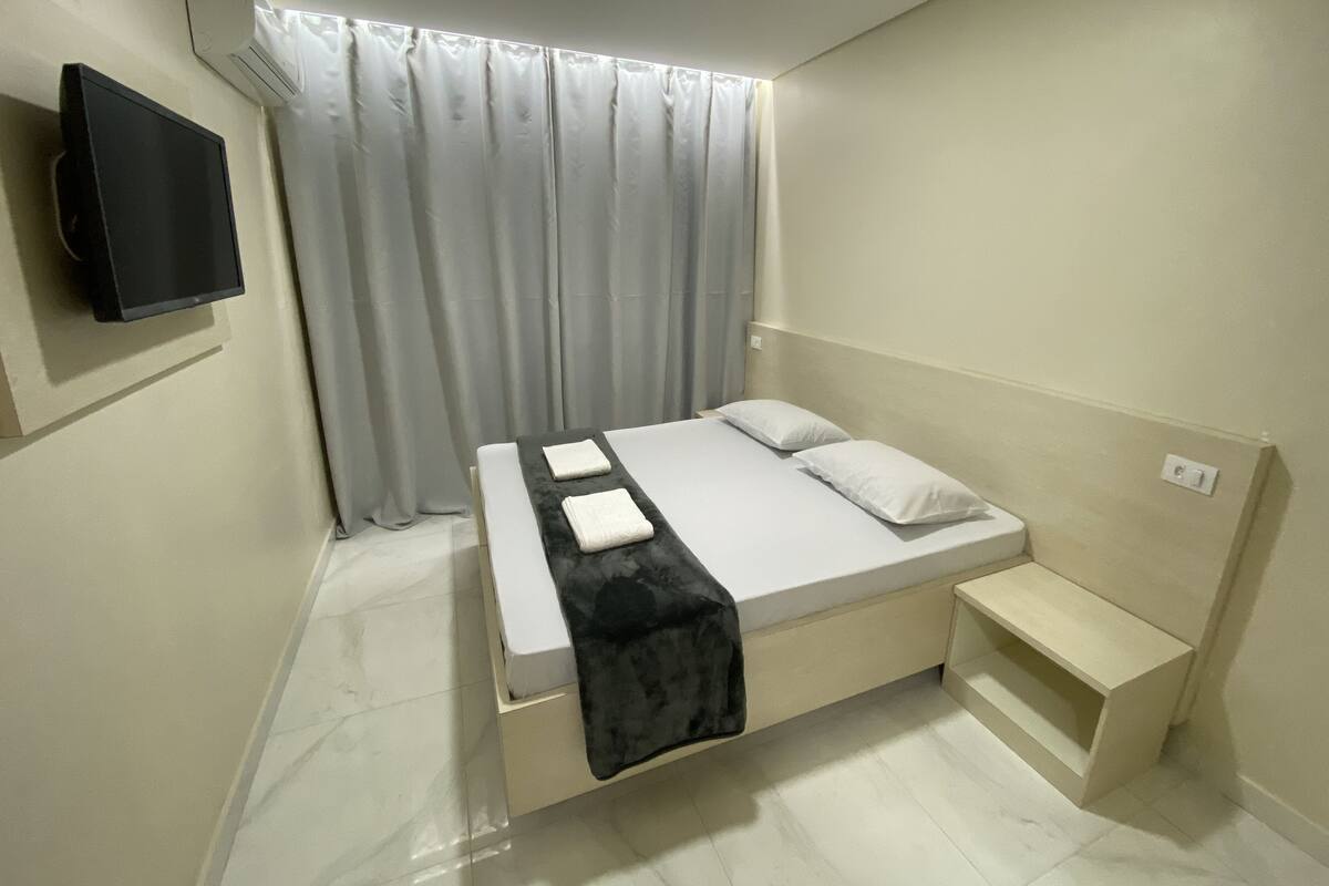 A modern bedroom with a bed, a TV mounted on the wall, and a window with curtains.