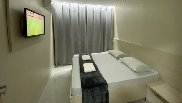 Una habitación de hotel moderna con una cama, un televisor montado en la pared y un ventanal con cortinas.
