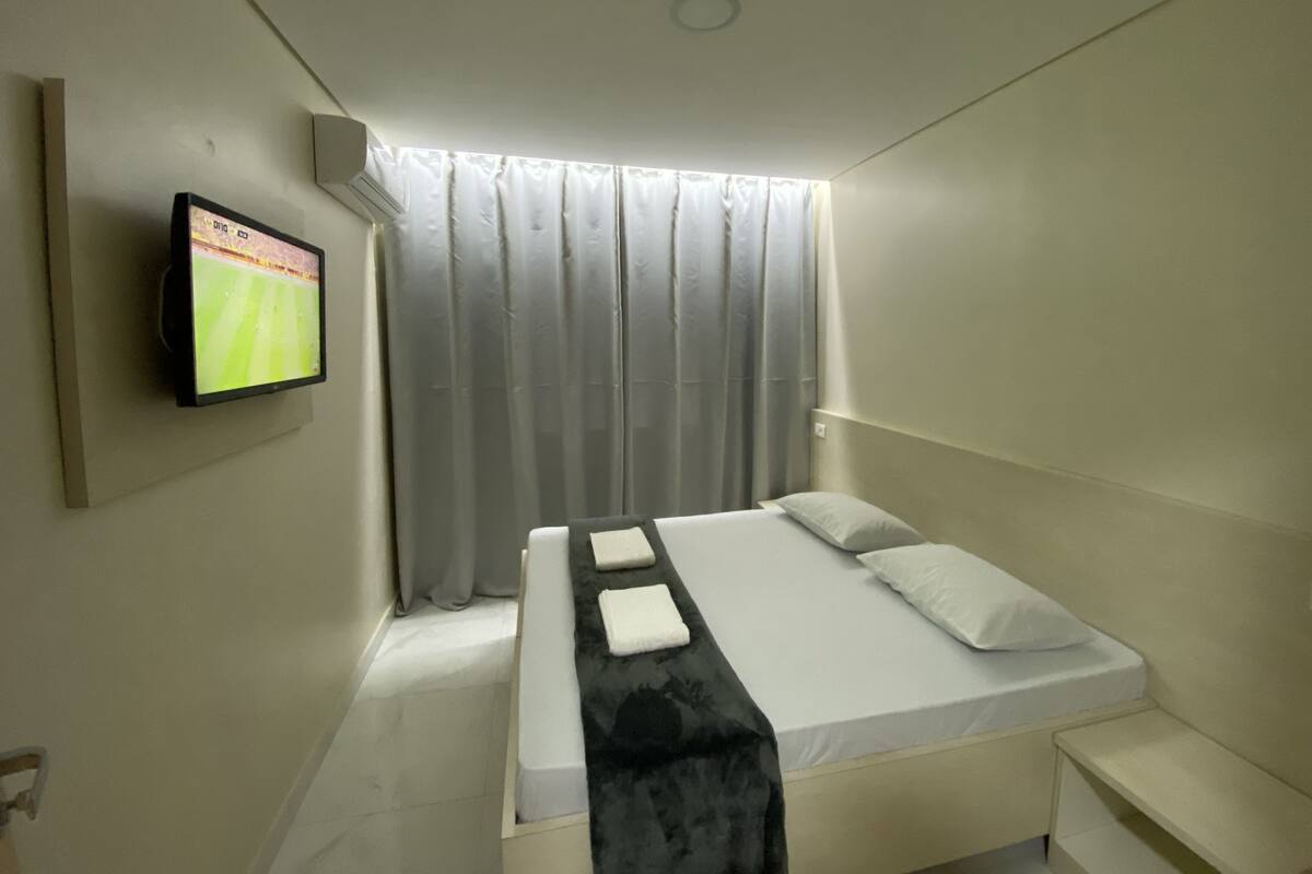 A modern hotel room with a bed, a TV mounted on the wall, and a window with curtains.