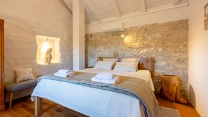 Une chambre avec un mur en pierre, un plancher en bois et un lit recouvert de draps blancs.