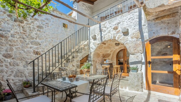 Une cour pavée de pierres, avec une table et des chaises, une porte en bois et un escalier.
