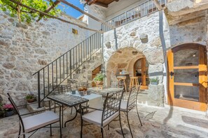 A stone courtyard with a table and chairs, a wooden door, and a staircase.