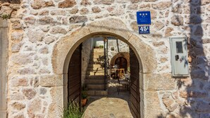 Un arc en pierre mène à une cour intérieure où se trouvent une table et des chaises, un panneau indiquant la chambre 45A, et un panneau d’information sur les règles de voyage de l’Union européenne.