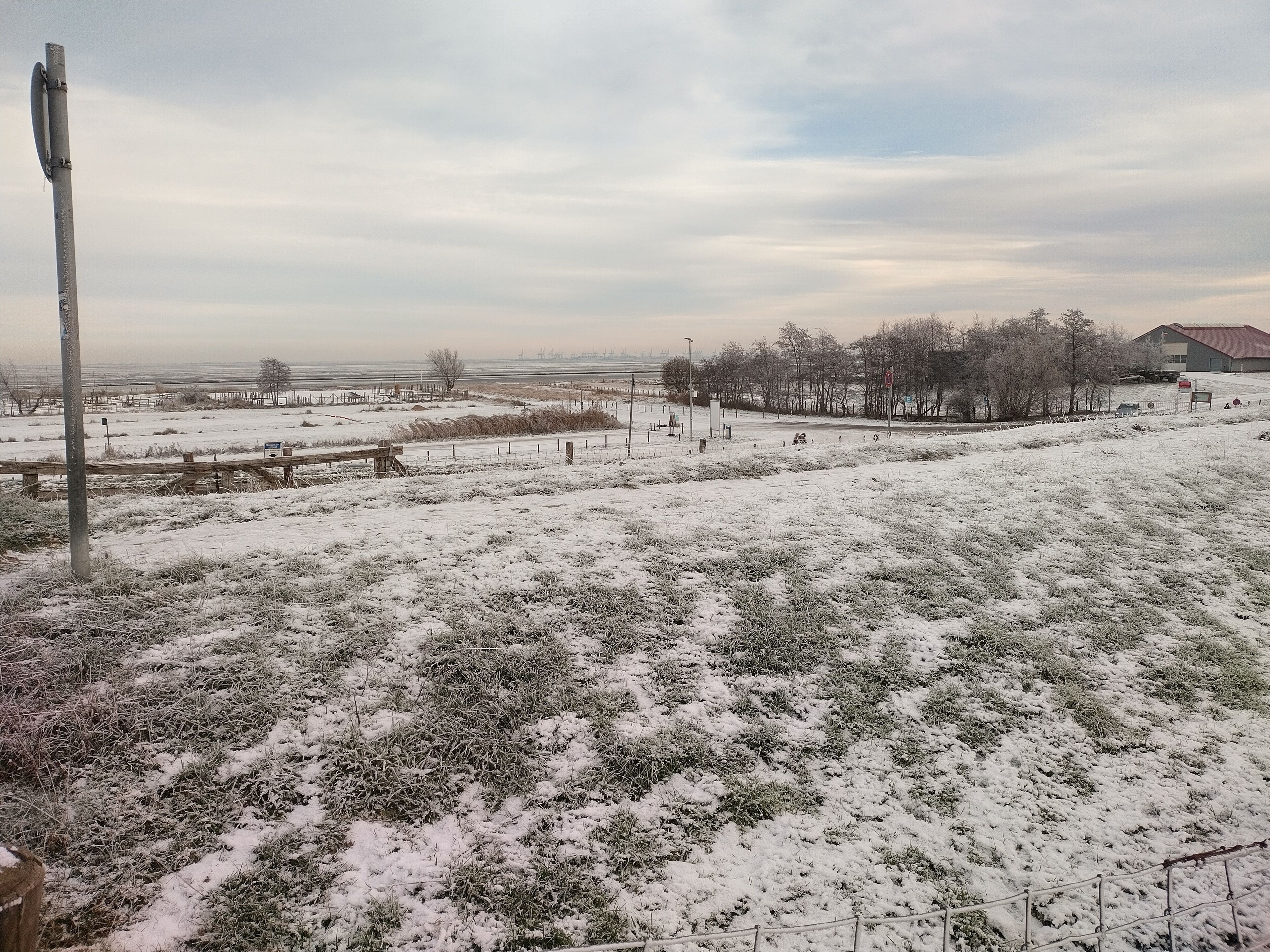 A snowy landscape with a fence, a utility pole, and a distant building.