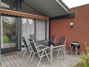 An outdoor patio with a glass table and chairs, a barbecue grill, and a brick wall.