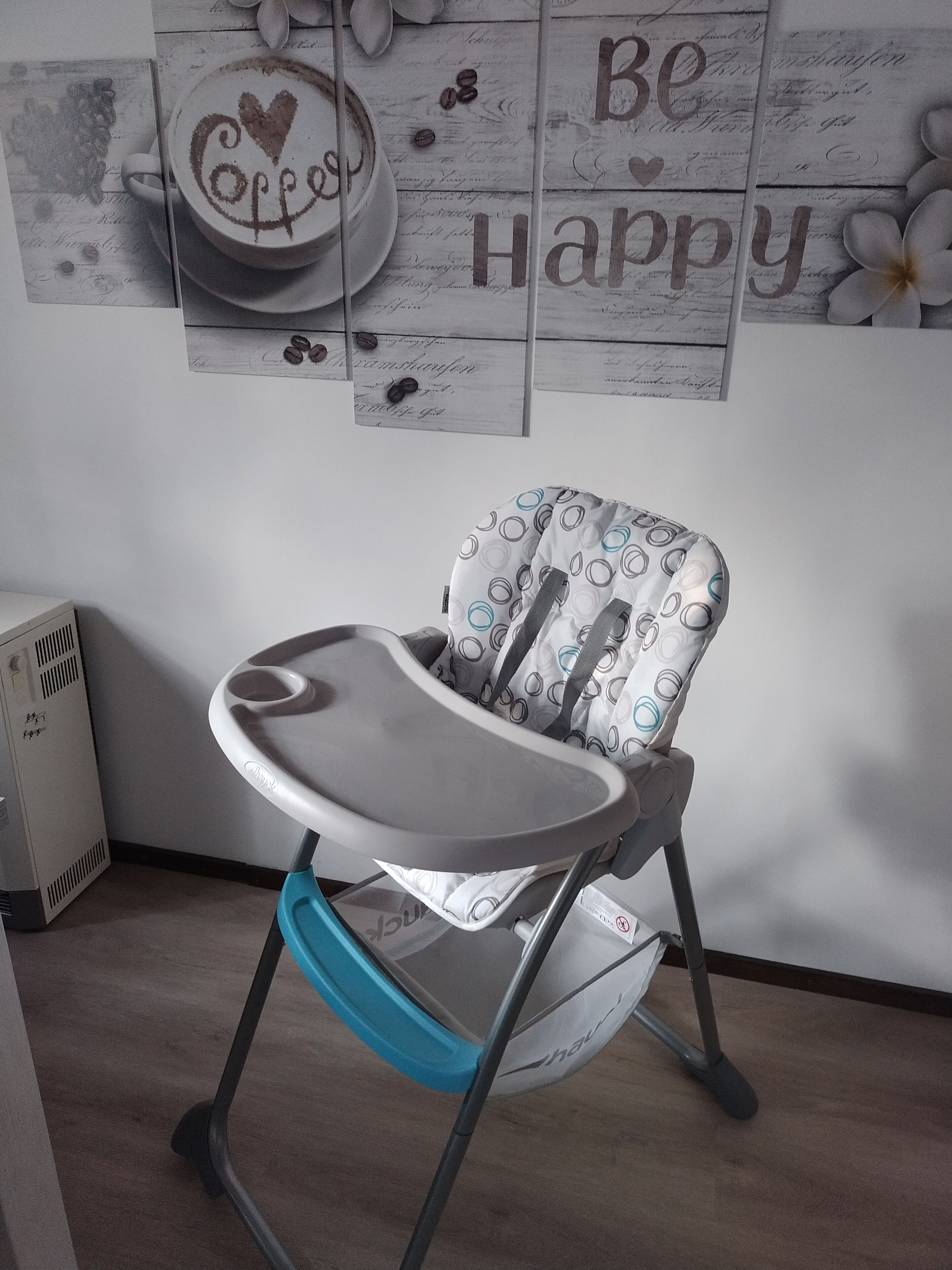 Una trona para bebés con bandeja, ubicada en una habitación con pared de madera y radiador.