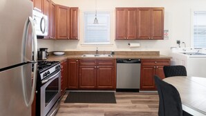 Cocina moderna con armarios de madera, electrodomésticos de acero inoxidable, un lavaplatos y una zona de comedor con mesa y sillas.