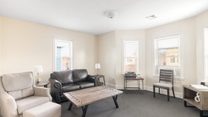 Una sala de estar con sofá, sillón, mesa de centro y una mesita auxiliar con lámpara.