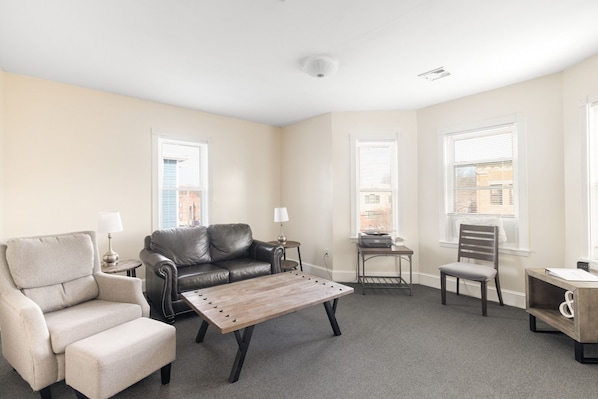 A living room with a sofa, armchair, coffee table, and a small side table with a lamp.
