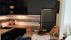 A modern kitchen with black cabinets, a wooden dining table set with blue plates, and a black refrigerator. - Paris - Porte D'auteuil : Grand Studio Avec Balcon (Paris)