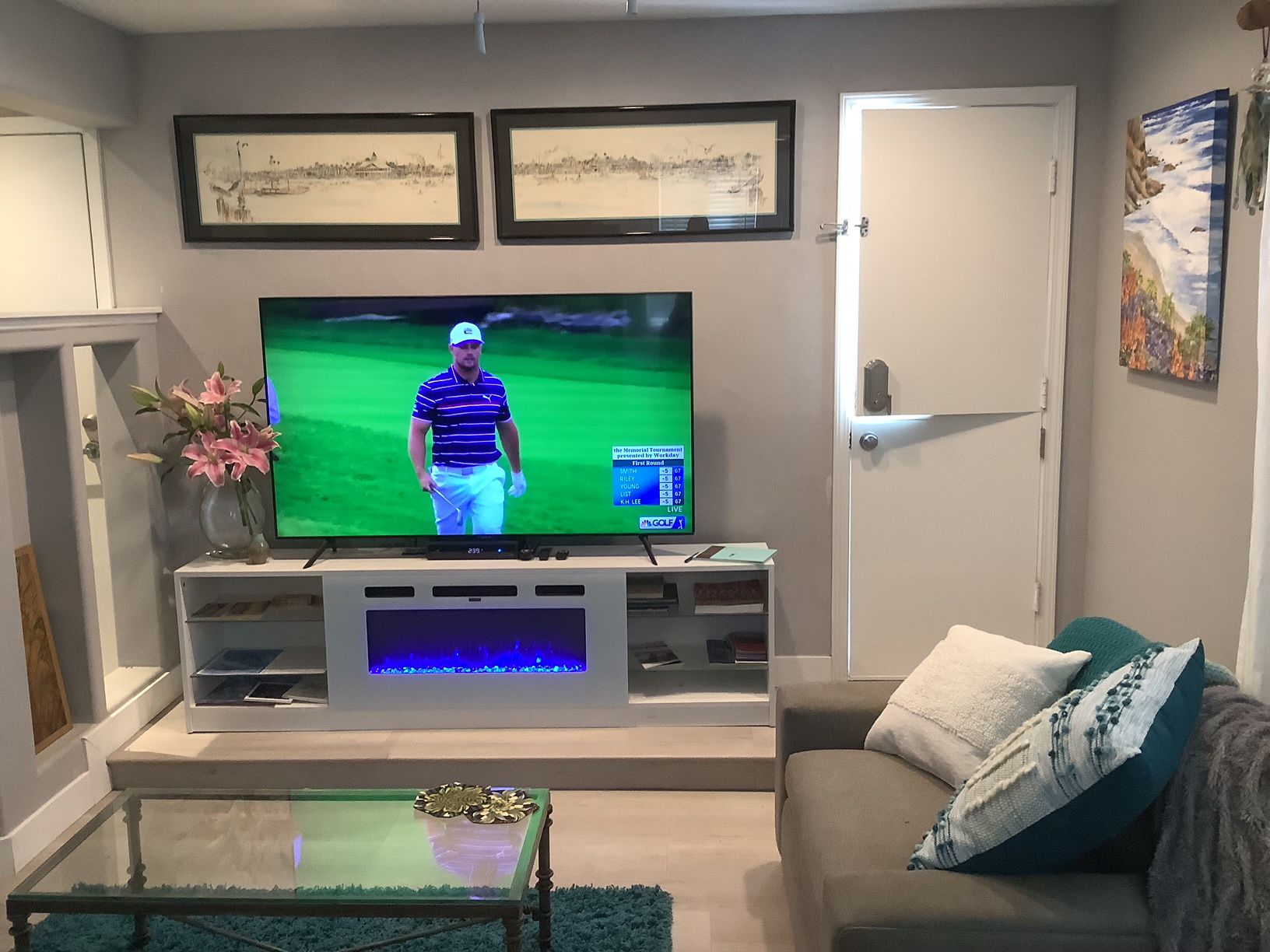 Una sala de estar con una televisión de pantalla plana sobre un mueble bajo, una mesa de centro de vidrio, un sofá y una puerta.