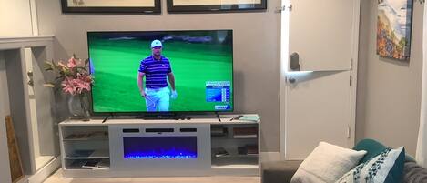 Una sala de estar con una televisión de pantalla plana sobre un mueble bajo, una mesa de centro de vidrio, un sofá y una puerta.