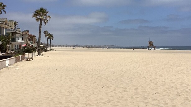 A beach with a lifeguard tower, palm trees, and beachfront houses.