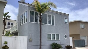 A two-story residential building with a gray facade, white-framed windows, and a palm tree in front.