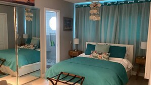 A bedroom with a large bed, a mirror, a wooden chair, and a nightstand with a lamp.