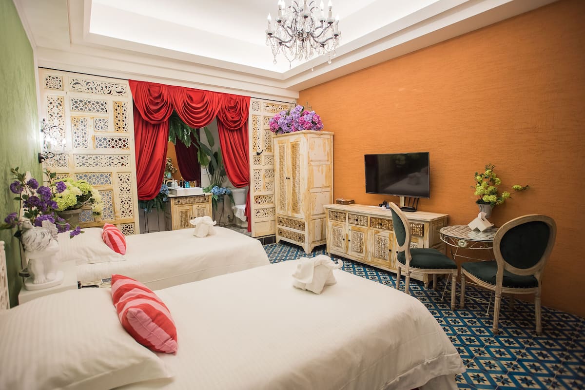 Hotellihuone, jossa on kaksi sänkyä, televisio, työpöytä tuolilla ja kattokruunu.