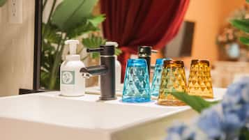 Una encimera de baño con dispensador de jabón, un grifo negro y una fila de recipientes de vidrio de colores.