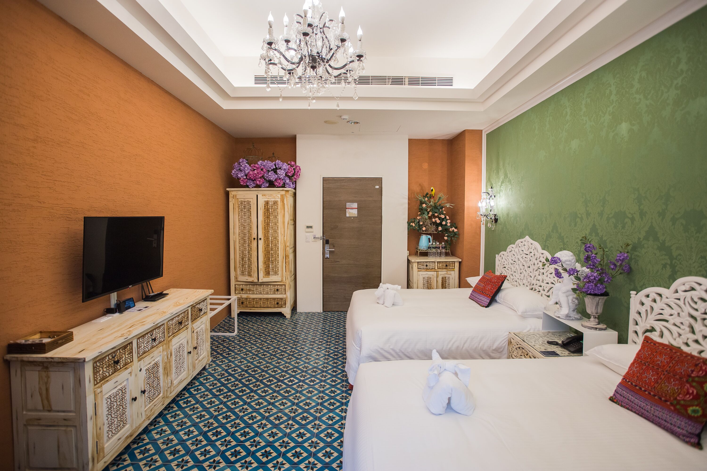 A hotel room with two beds, a television, a cabinet with decorative items, and a patterned floor.
