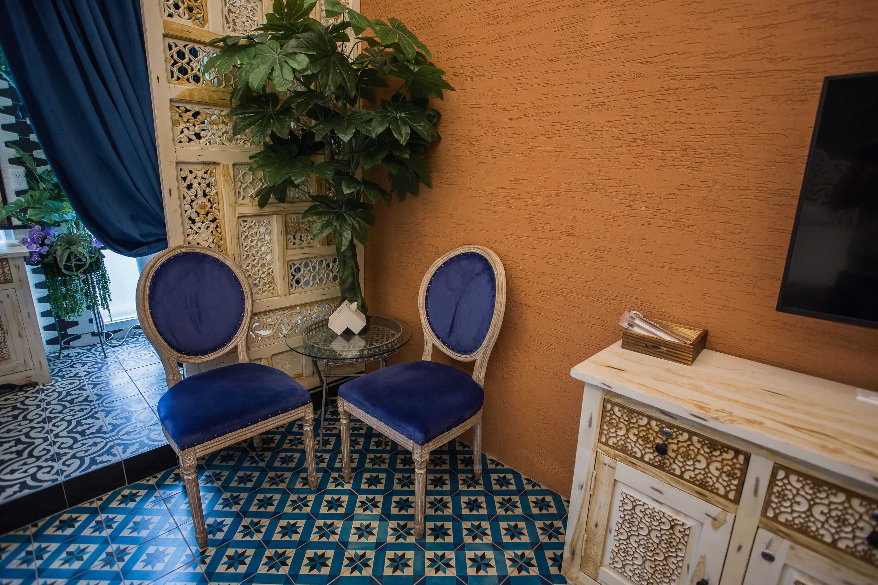 A room with two blue upholstered chairs, a small round table, and a decorative cabinet.