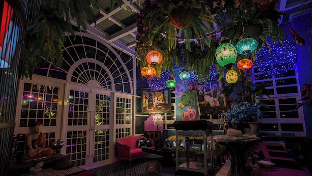 Une véranda dotée d’un toit en verre, de plantes d’intérieur et de lanternes suspendues.