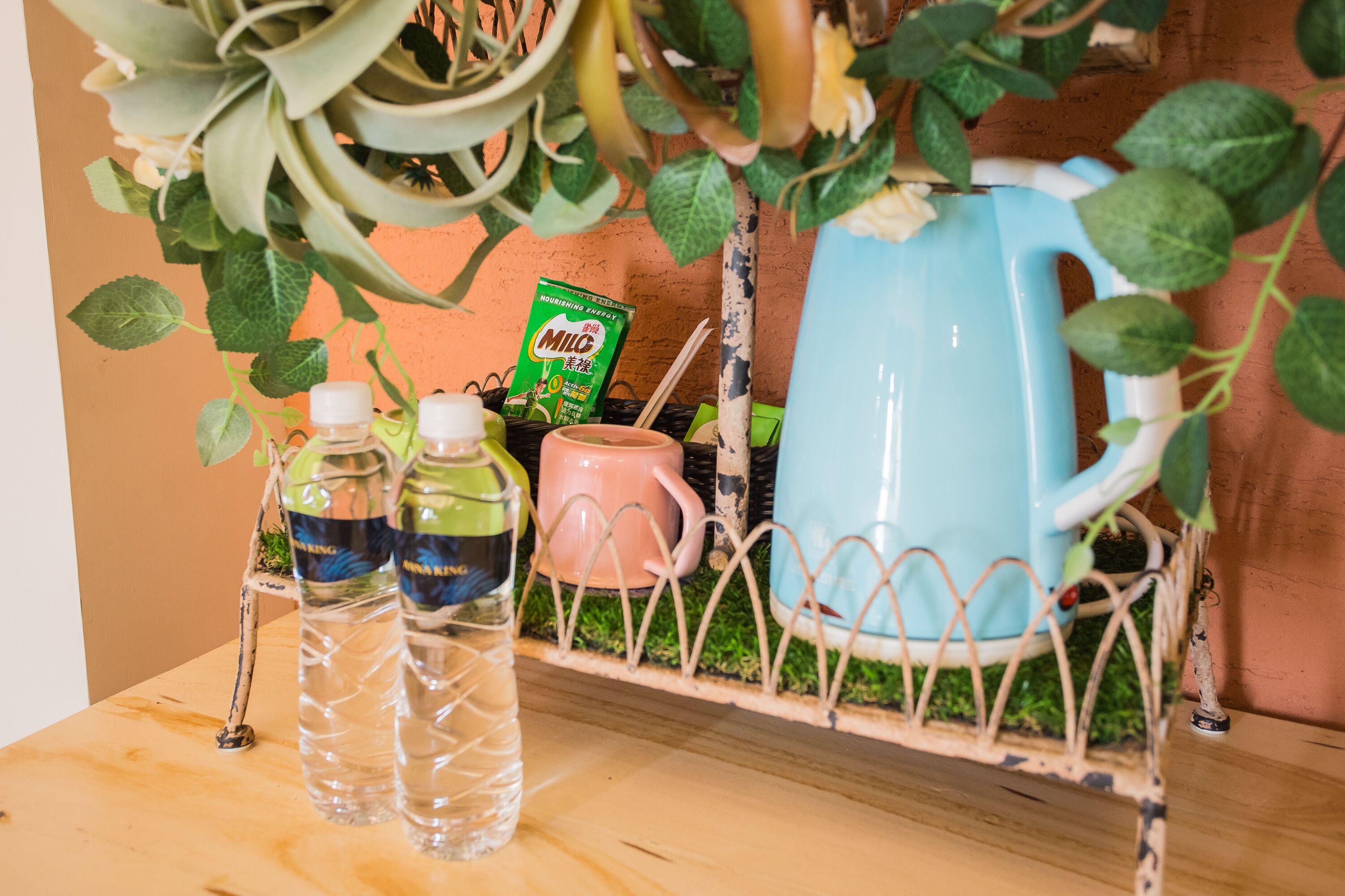 A rustic kitchen area with a wooden table, two water bottles, a pink mug, a green milk carton, and a blue pitcher.