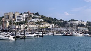 A marina with multiple boats docked, surrounded by buildings and a hilly backdrop. - Luxury 3 bed apartment a few minutes walk from beach, harbour and town! (Torquay)