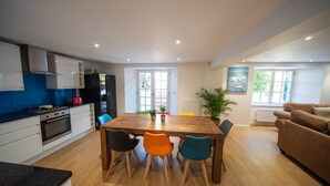 A modern kitchen with white cabinets, a stove, and a dining area with a wooden table and colorful chairs. - Luxury 3 bed apartment a few minutes walk from beach, harbour and town! (Torquay)