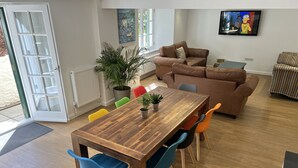 A modern living room with a wooden dining table, colorful chairs, a brown sofa, and a television on the wall. - Luxury 3 bed apartment a few minutes walk from beach, harbour and town! (Torquay)