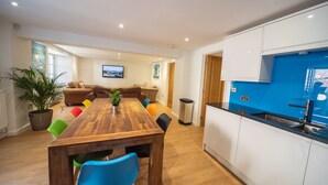 A modern living room with a wooden dining table, colorful chairs, a sofa, and a large potted plant. - Luxury 3 bed apartment a few minutes walk from beach, harbour and town! (Torquay)