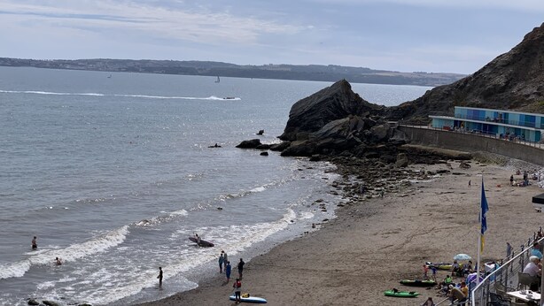 A beach with a rocky outcrop, a pier, and a building with a blue facade. - Luxury 3 bed apartment a few minutes walk from beach, harbour and town! (Torquay)