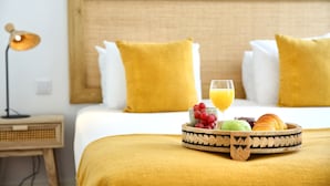 A neatly made bed with a yellow blanket, a bedside table with a lamp, and a fruit and juice tray on the bed.