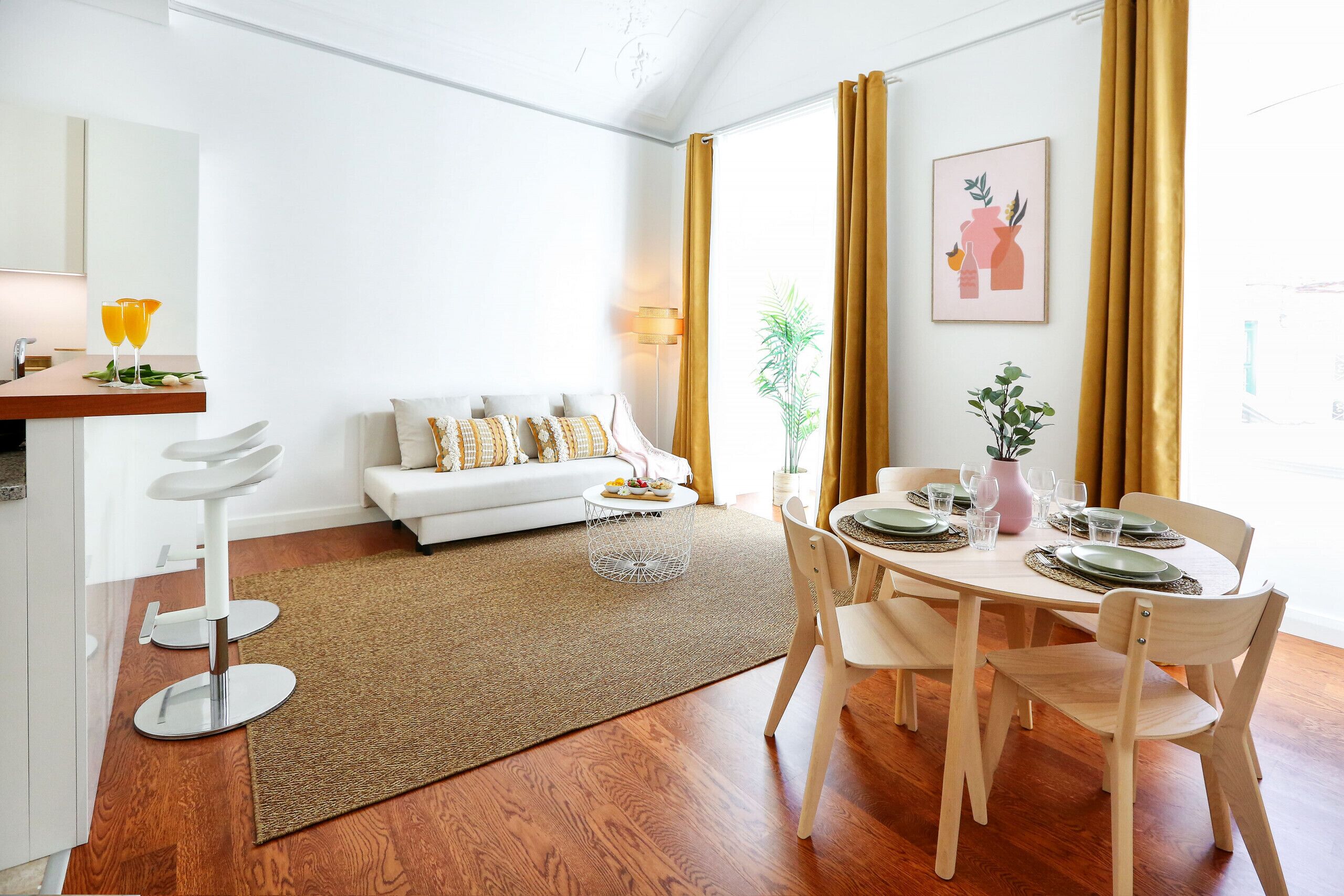 Una sala de estar moderna con un sofá blanco, una mesa de comedor preparada para cuatro personas y una zona de cocina con un taburete de bar.