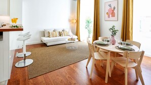 A modern living room with a white sofa, a dining table set for four, and a kitchen area with a bar stool. - Endless Summer Apartment (Faro)
