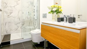 A modern bathroom with a glass shower enclosure, a white toilet, and a wooden vanity with a mirror. - President Pais Apartment (Faro)