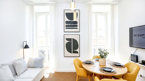 A modern living room with a sofa, a dining table with yellow chairs, and two abstract paintings on the wall. - President Pais Apartment (Faro)