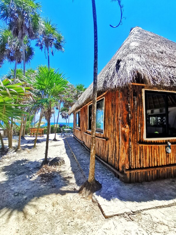 A wooden building with a thatched roof, surrounded by palm trees and a sandy beach.