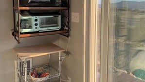 Una cocina con microondas integrado y repisa para horno, un carrito pequeño con toallas, y vistas a un paisaje montañoso a través de una puerta corrediza de vidrio.