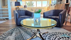 A modern living room with two dark armchairs, a glass coffee table, and a patterned rug.