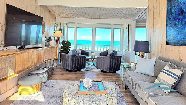 A spacious living room with a large TV, comfortable seating, a view of the ocean, and wooden walls.