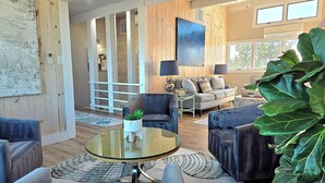 A spacious living room with a large sofa, a glass coffee table, and a large plant.