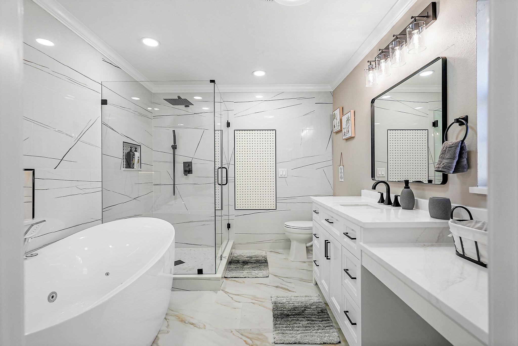 A modern bathroom with a freestanding bathtub, a glass-enclosed shower, a toilet, and a vanity with a large mirror.