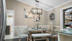 Un comedor con una mesa de madera, sillas acolchadas y una lámpara de araña.