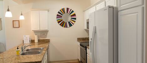 Una cocina con armarios blancos, encimera de granito, electrodomésticos de acero inoxidable y un colorido adorno circular en la pared.