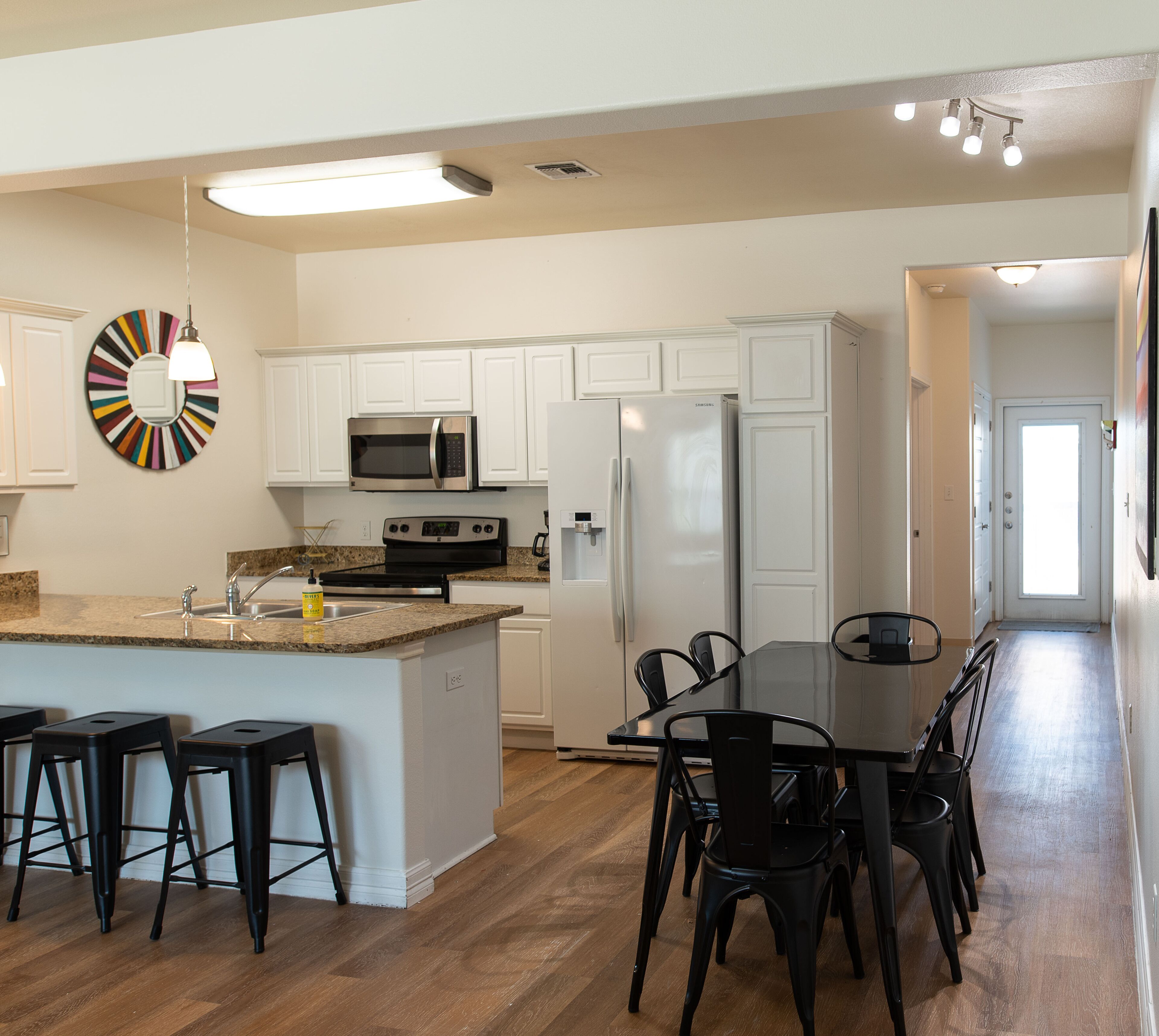 A modern kitchen with white cabinets, a stainless steel microwave, a refrigerator, and a dining area with a table and chairs.