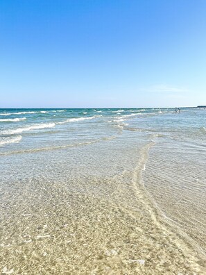 A beach with clear shallow waters and pebbles.