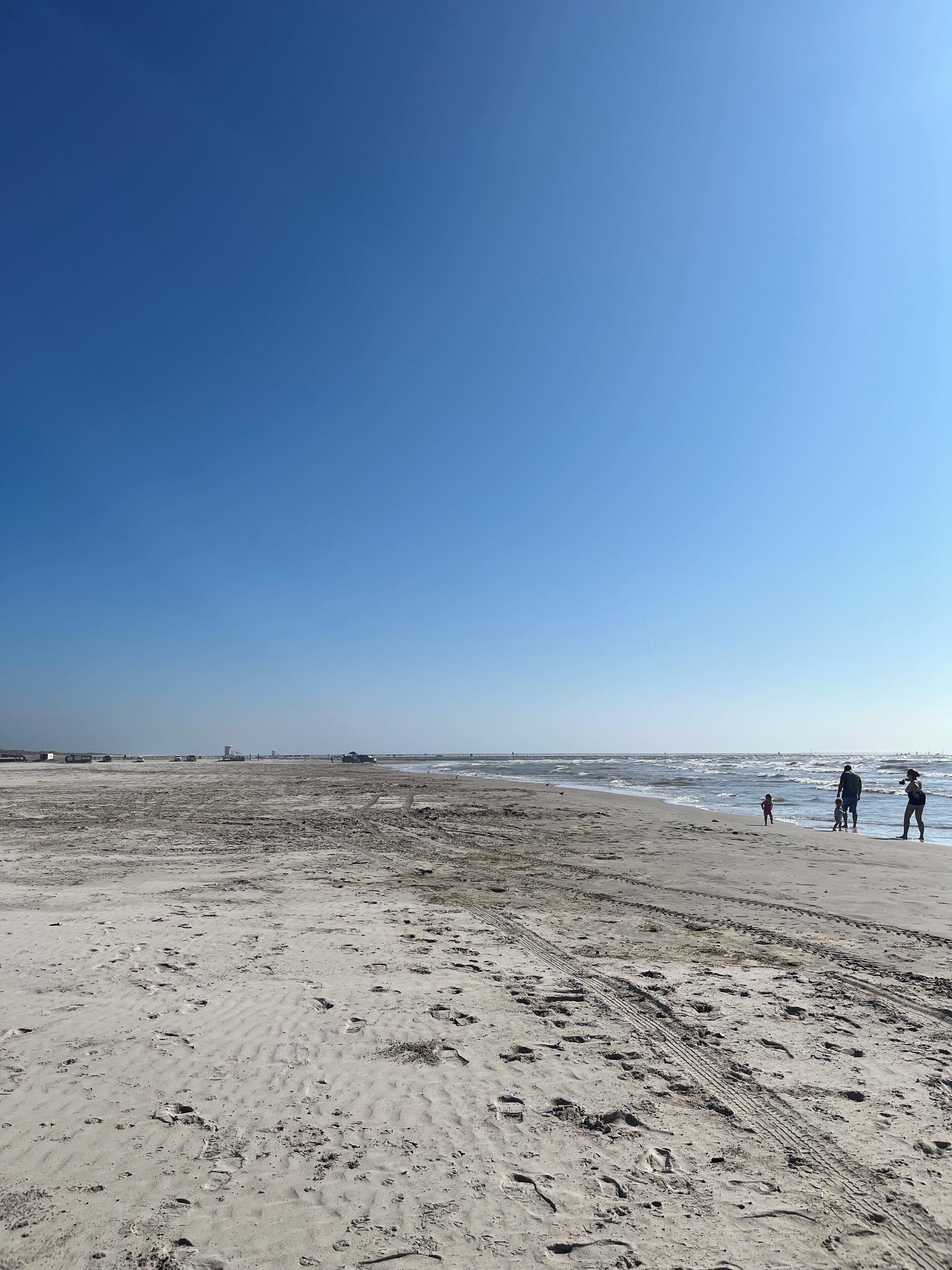 A wide sandy beach with footprints and tire tracks.