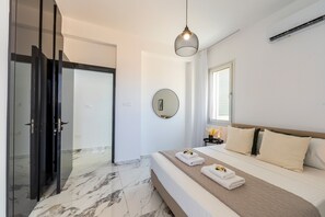 A modern bedroom with a bed, a bedside table, a mirror, and a door leading to a bathroom. - Protaras Sol e Mar Villa 3 (Protaras)