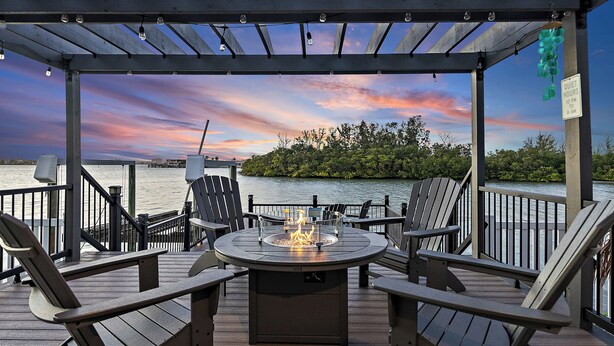 Una terraza con sillas Adirondack, un brasero y vistas a un cuerpo de agua al atardecer.