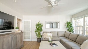 Ein modernes Wohnzimmer mit Flachbildfernseher, Deckenventilator, einer Couch, einem Couchtisch und zwei Topfpflanzen.